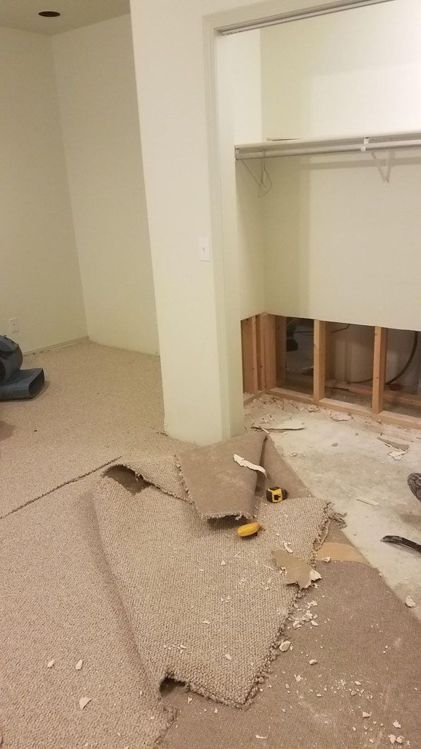 Damaged room with torn carpet, exposed wall studs, and debris on the floor.