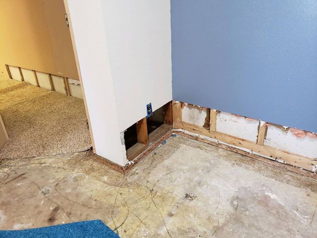 Empty room with removed baseboards, exposing wall framing and unfinished flooring along a corner.