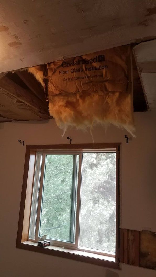 Damaged ceiling with exposed insulation above a window in a room