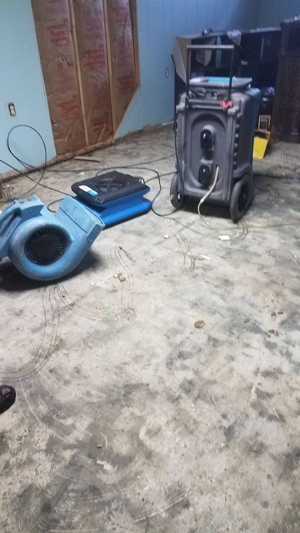 Blue speaker and audio equipment on a dirty floor in a cluttered room.