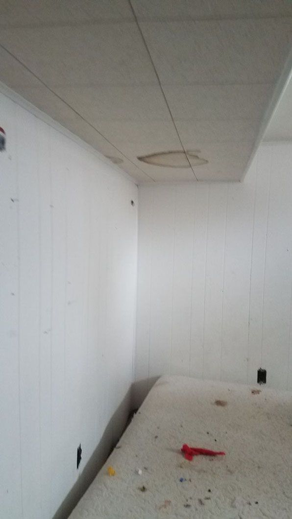 Empty white room with drop ceiling, unfinished walls, and debris on the floor.