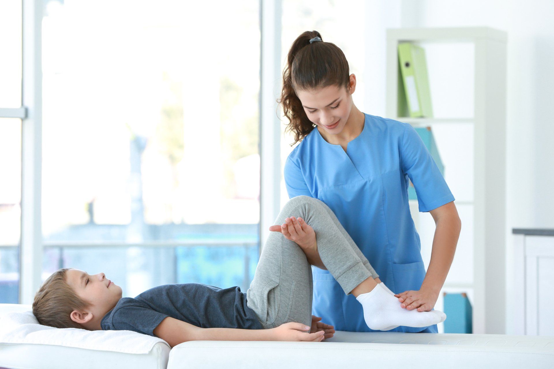 Un jeune garçon est allongé sur un lit pendant qu'une infirmière lui tend la jambe.