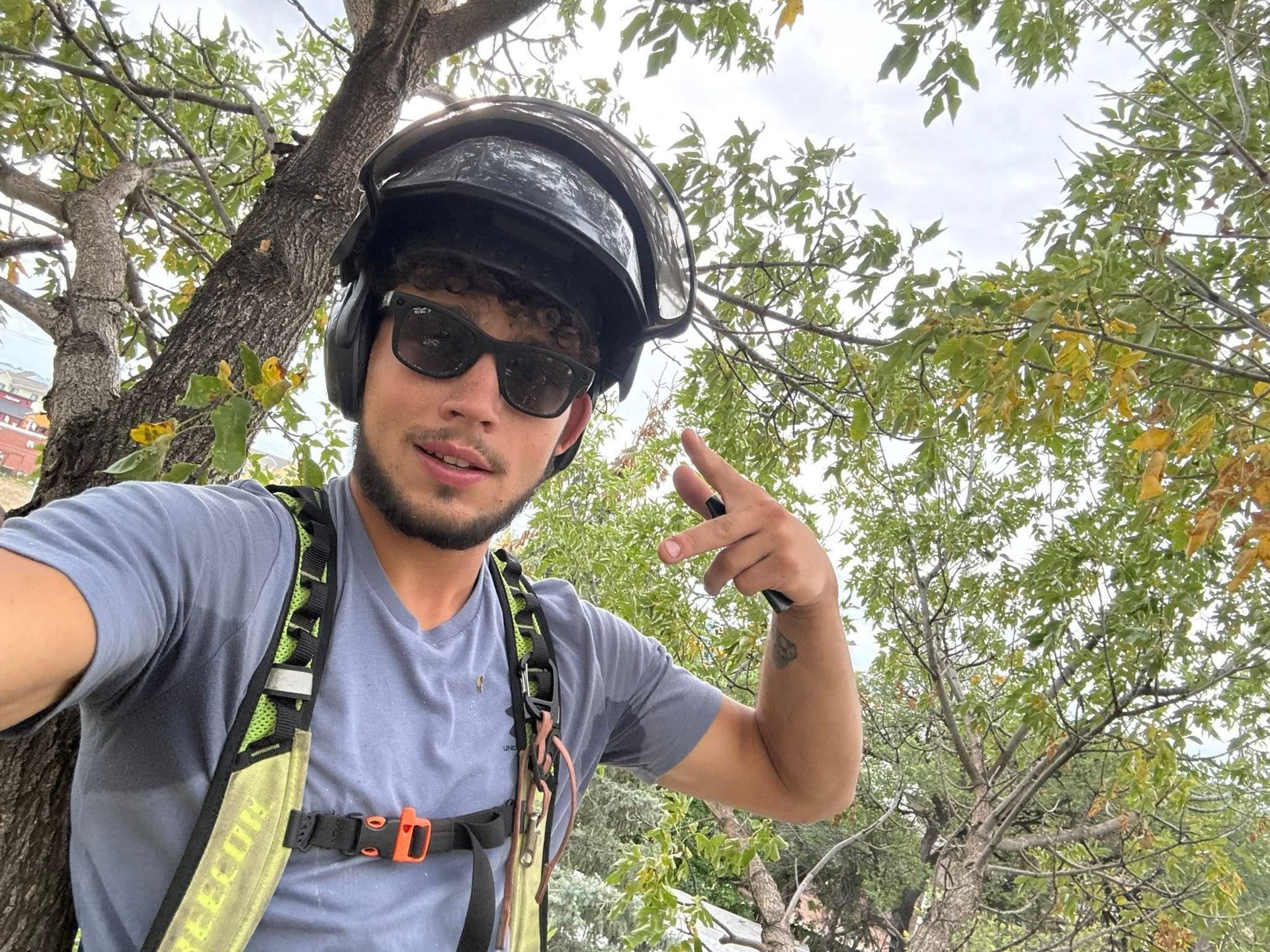Selfie of a cyclist wearing a helmet and sunglasses, flashing a peace sign in a leafy outdoor setting