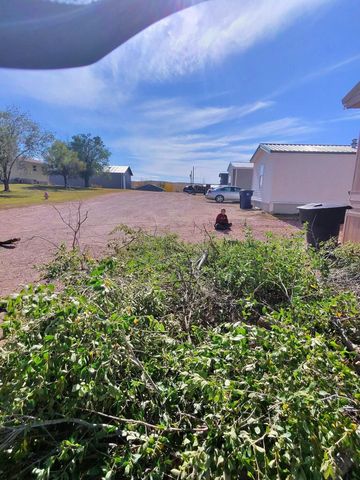 Gravel road beside white trailers under a blue sky, with a person in red in the distance and green shrubs in front.