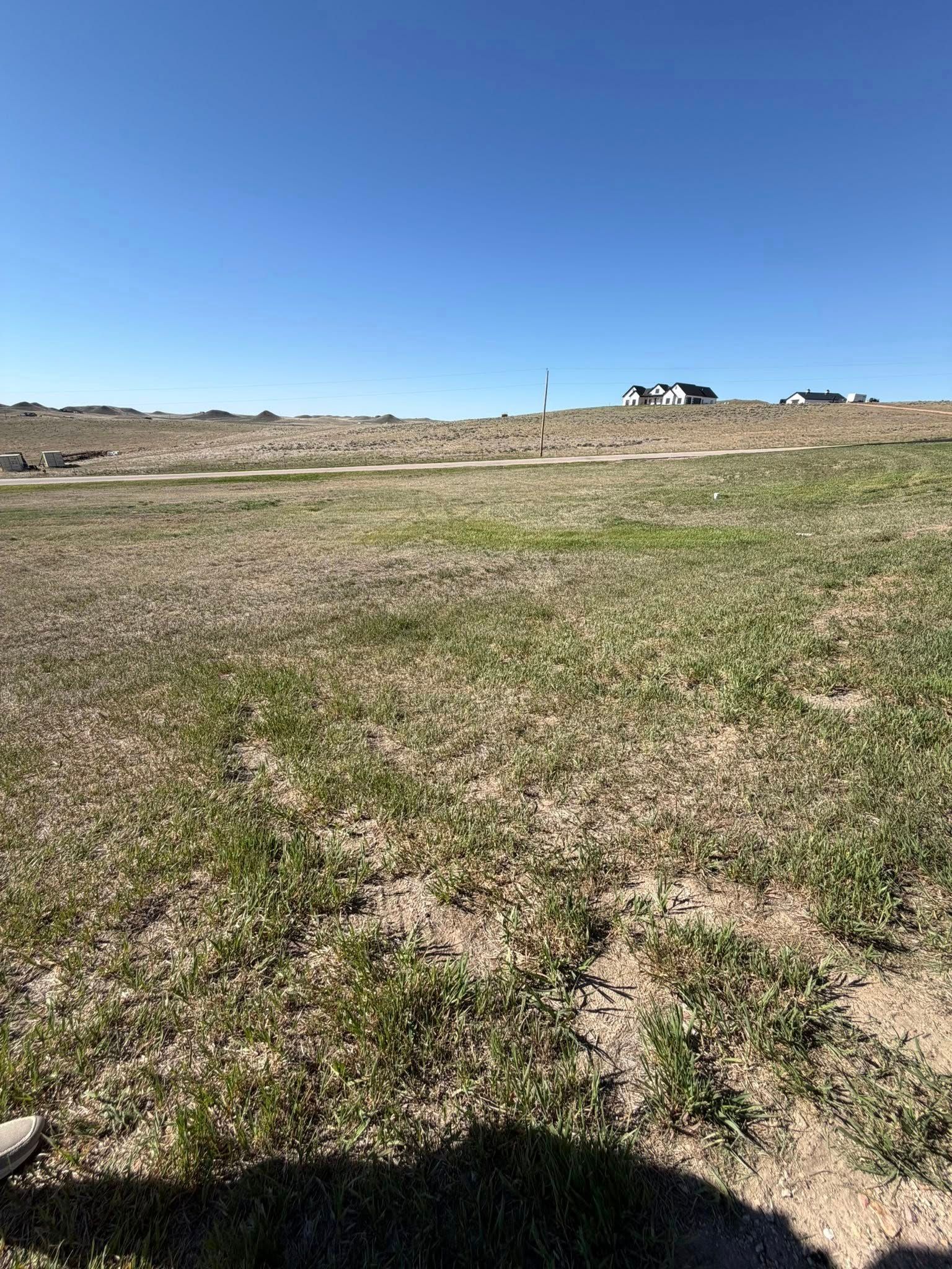 Open grassy field under a clear blue sky with buildings on the horizon