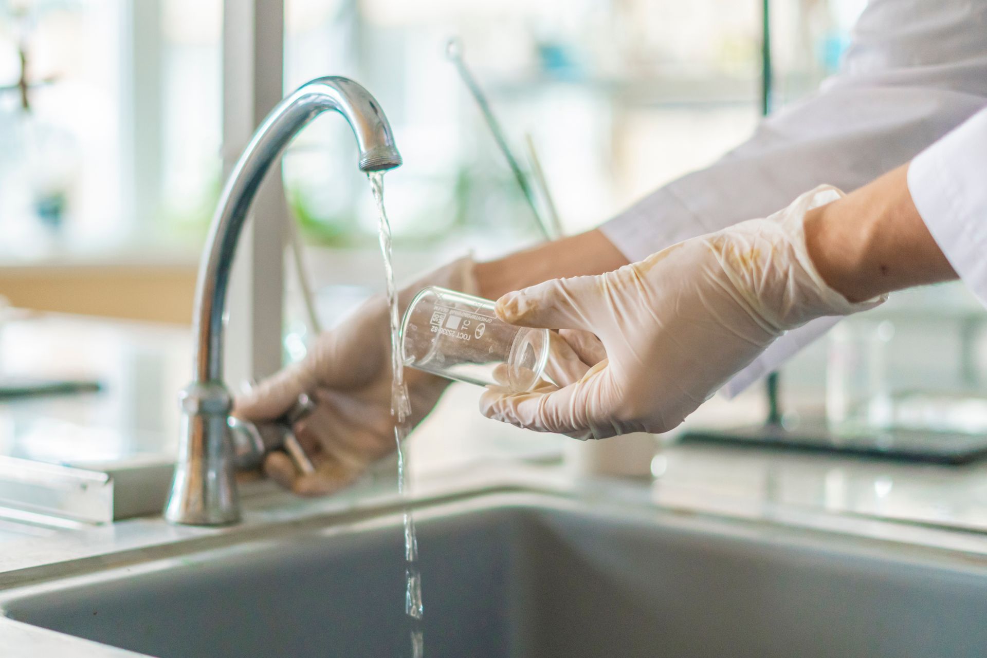 Gloved hands rinsing a glass under a kitchen faucet with running water