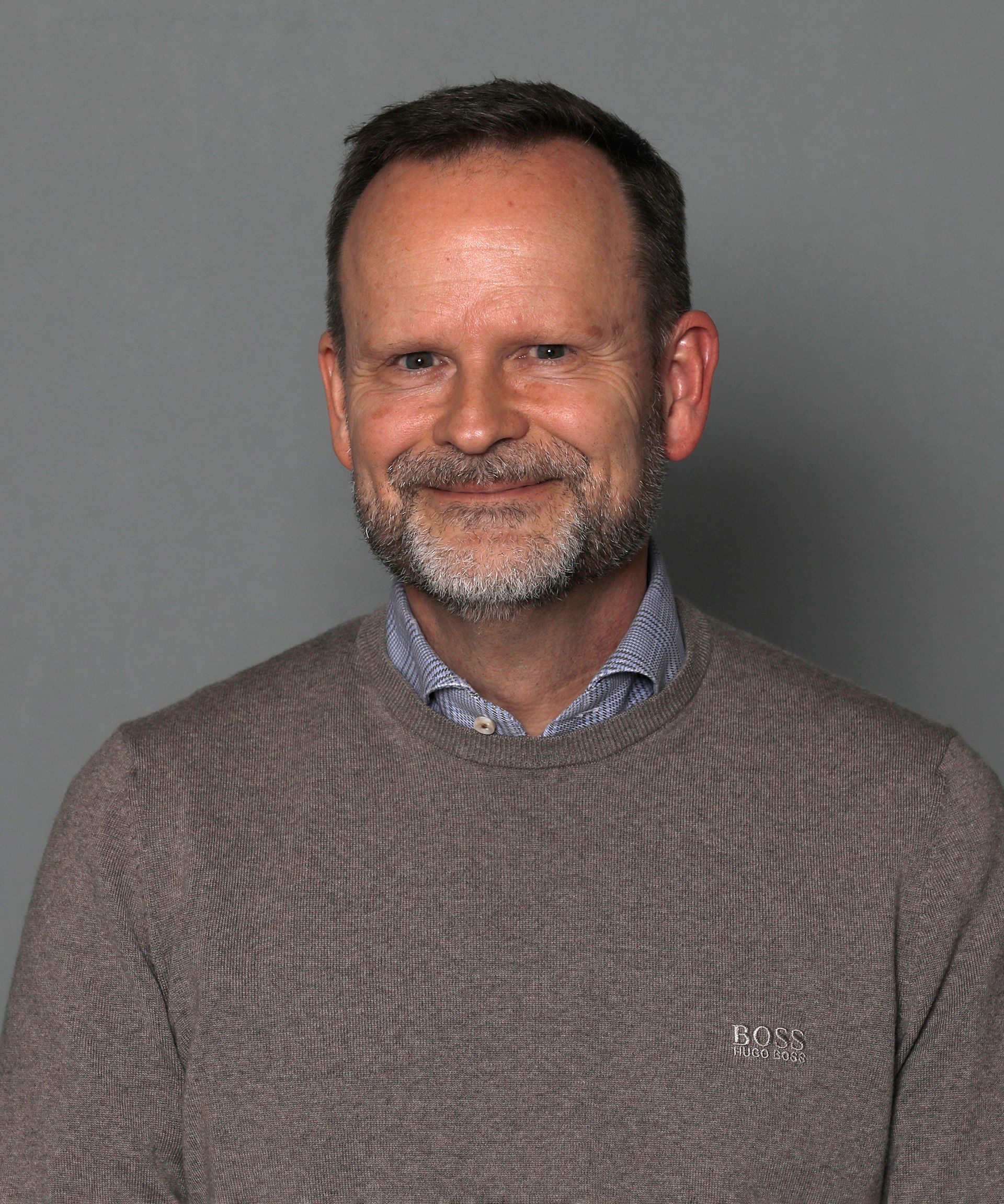 Man smiling in a gray sweater against a plain gray background