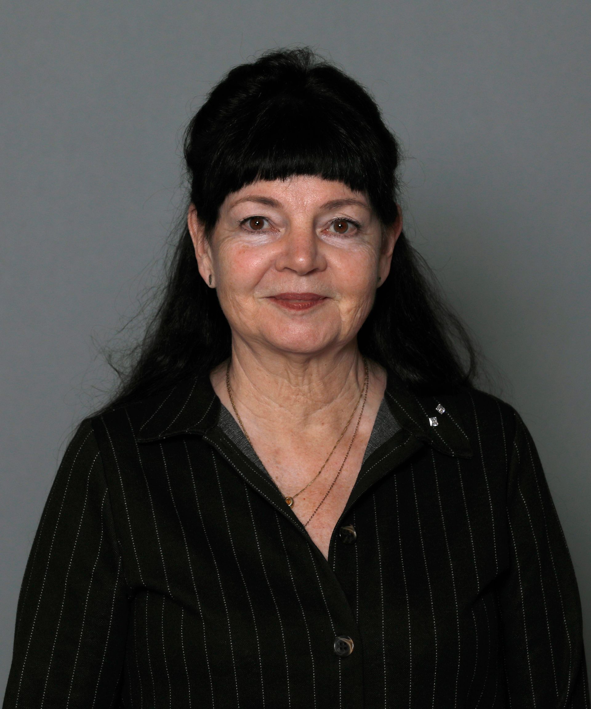 Woman with dark hair wearing a black blouse, smiling against a gray background