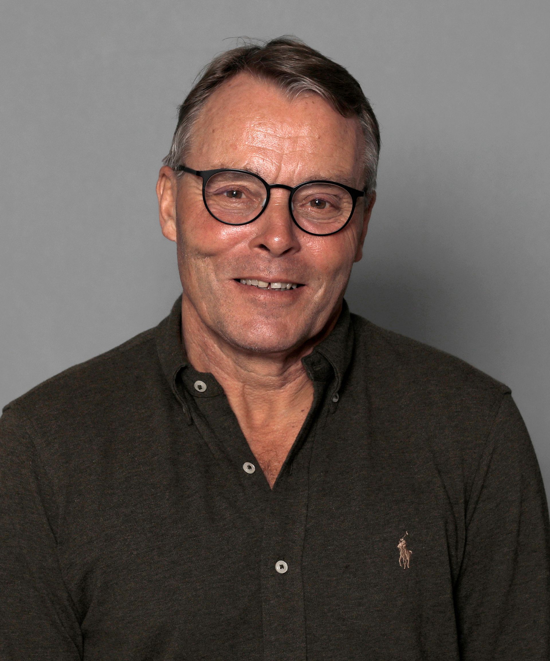 Portrait of a smiling man wearing glasses and a dark polo shirt against a gray background