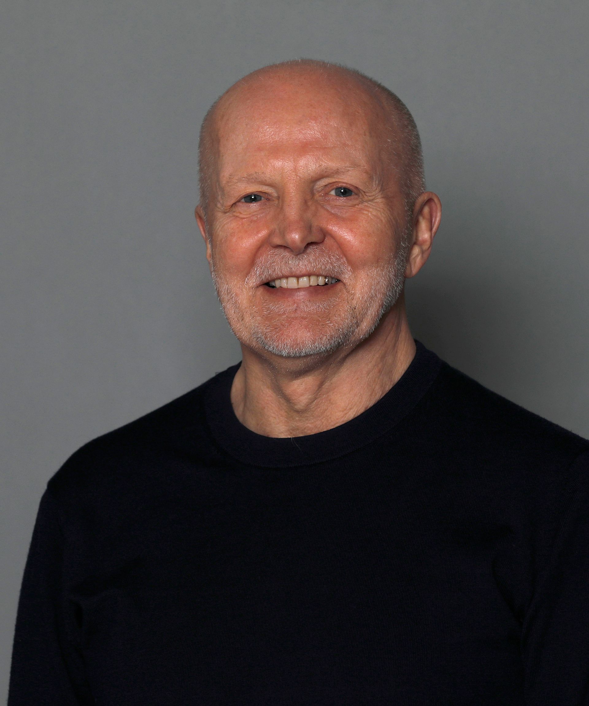 Smiling bald man in a black shirt against a gray background