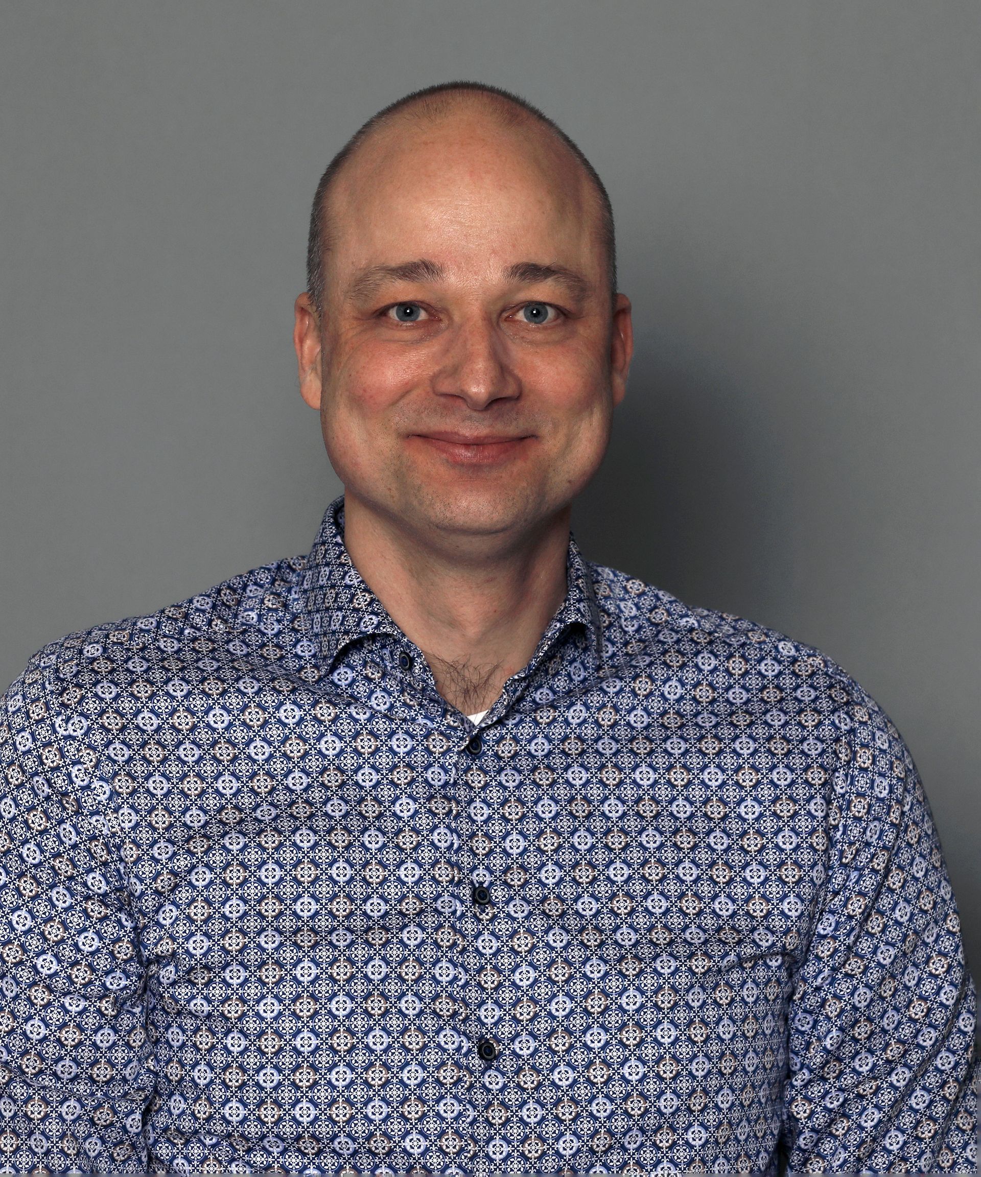 Smiling bald man in a blue patterned shirt against a gray background