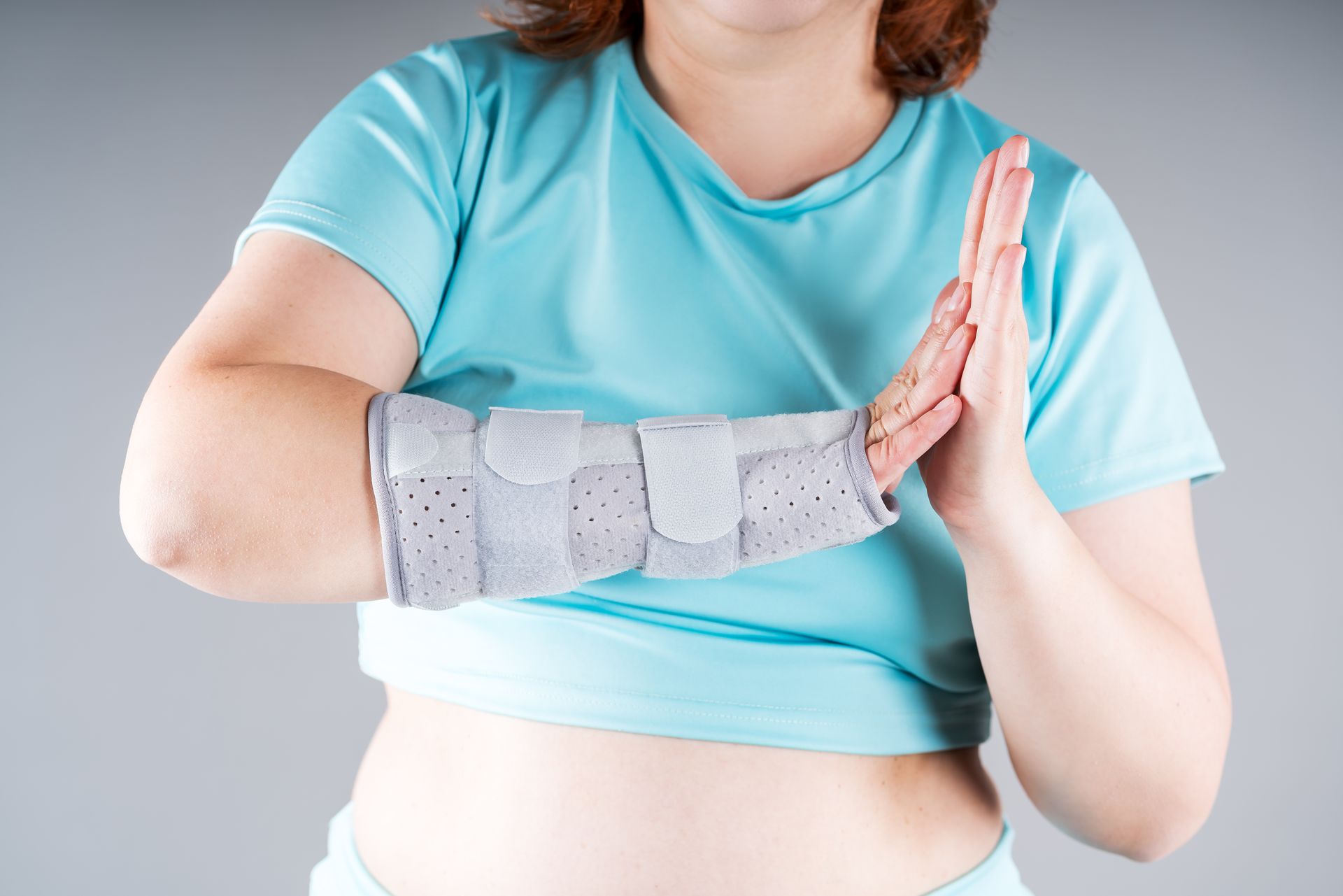 Person wearing a gray wrist brace holds a pink hand brace against a light blue shirt.