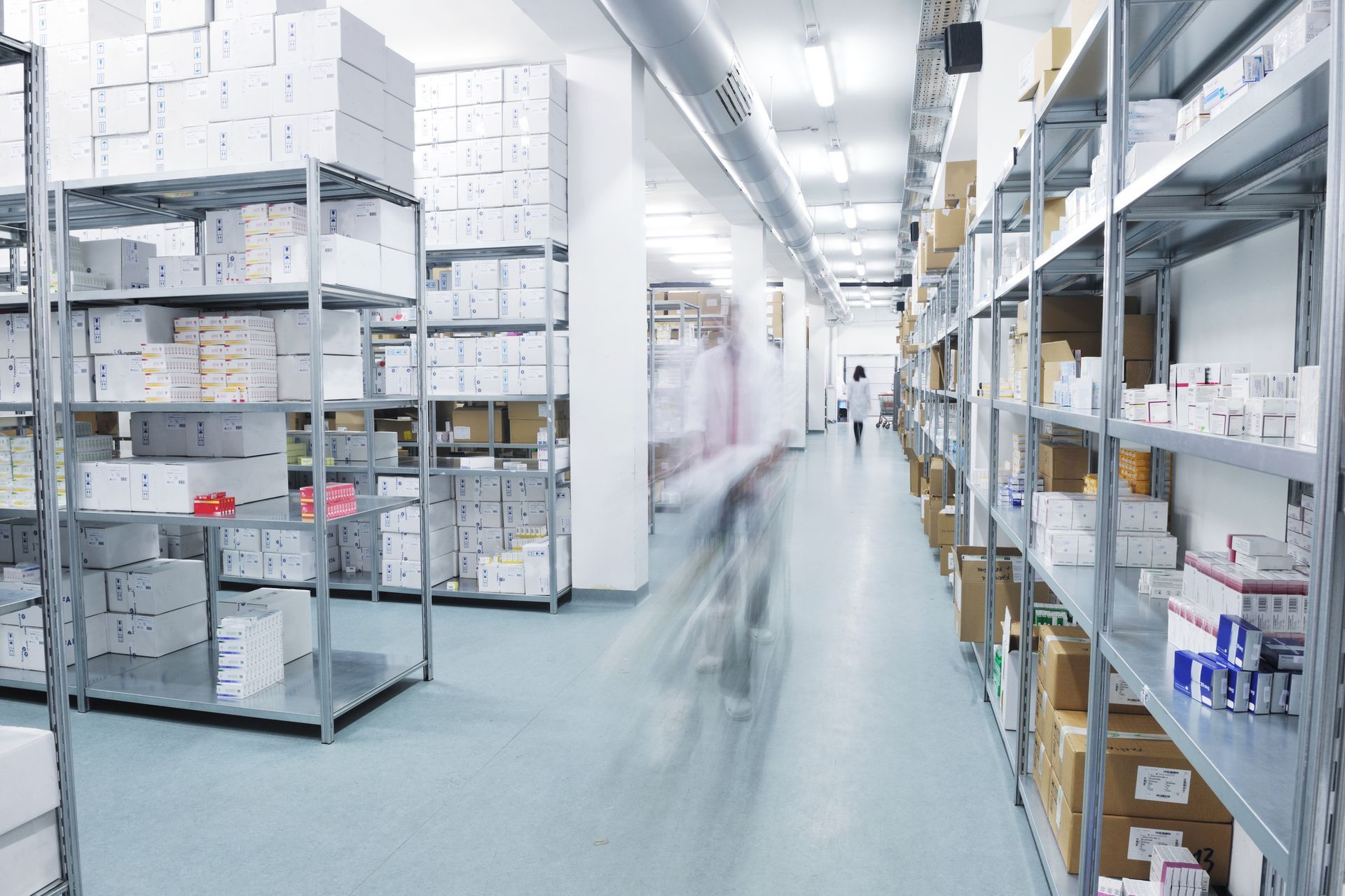 Staff walking through a medical supply warehouse with shelves of boxes.