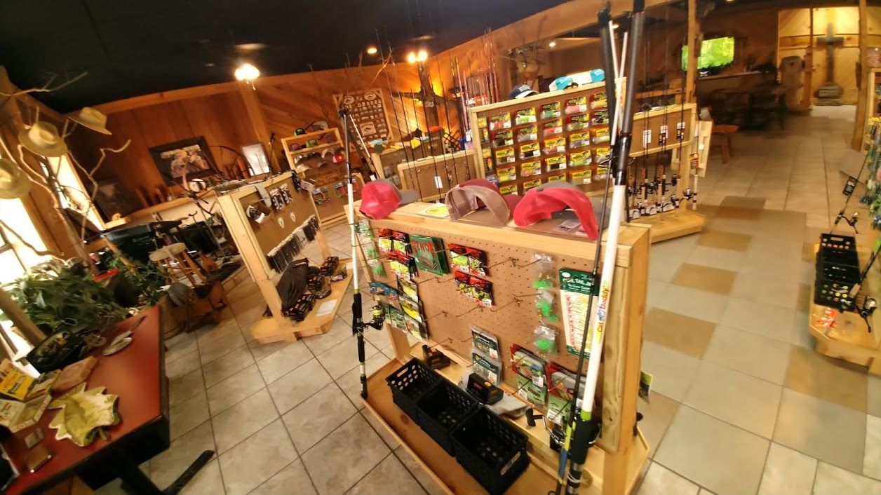 Interior view of a rustic shop with wooden displays, shelving units, and fishing gear, featuring tiled flooring.