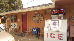 A tan building exterior with a red door, outdoor seating, and an ice machine under an