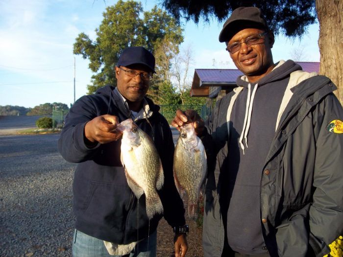 Two people standing outdoors, each holding up a fish they have caught.