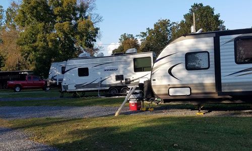 Several recreational vehicles parked on a gravel lot under a clear blue sky with trees in the background.