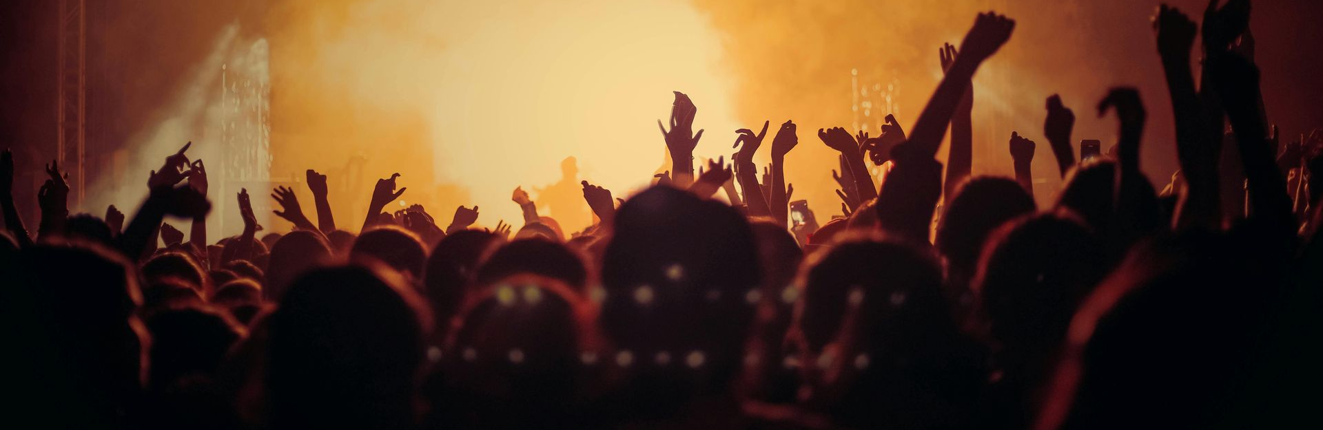 A crowd with raised hands at a concert, lit by bright stage lights.
