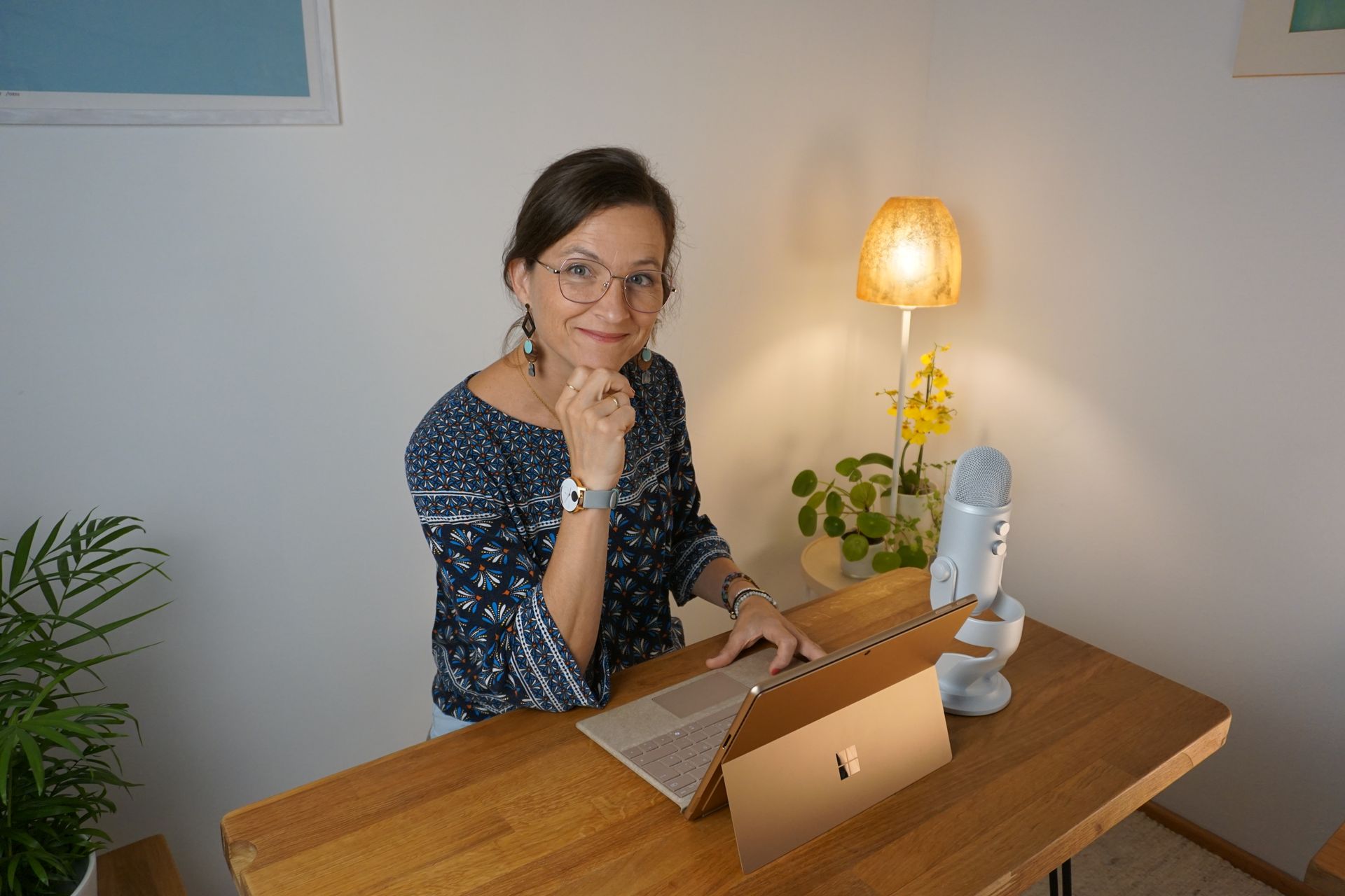 Frau an einem Holzschreibtisch, die in einem schwach beleuchteten Heimbüro einen Laptop und ein Tablet benutzt