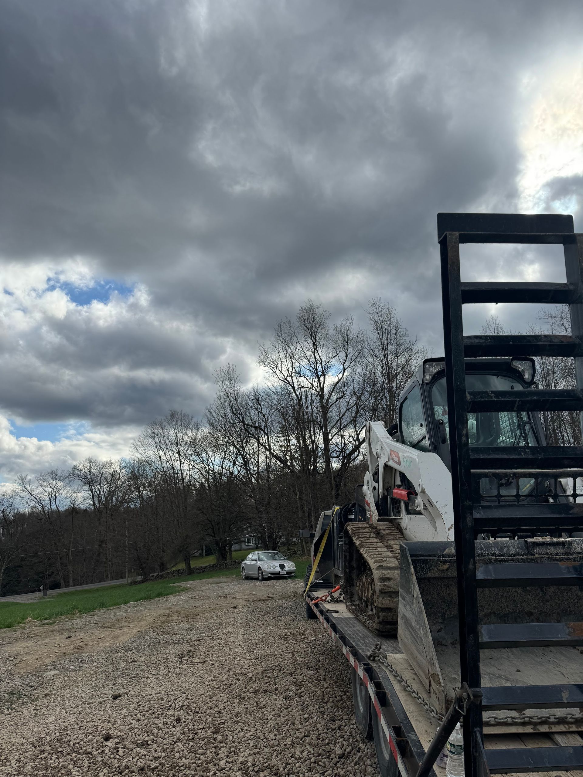 A bulldozer is sitting on top of a trailer on a gravel road.