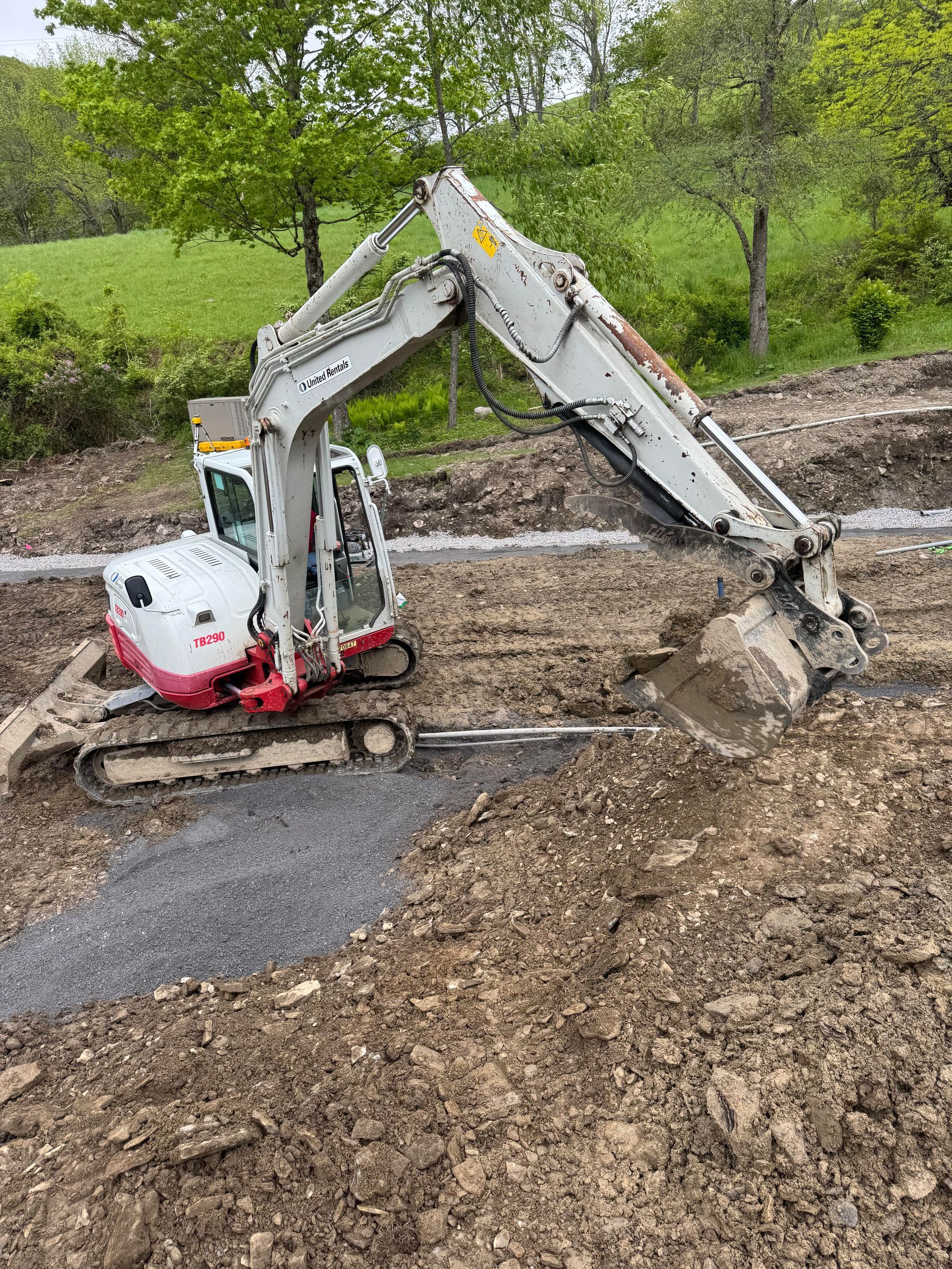 Excavator digging into a muddy ground, gray gravel alongside it. White and red machine outdoors.