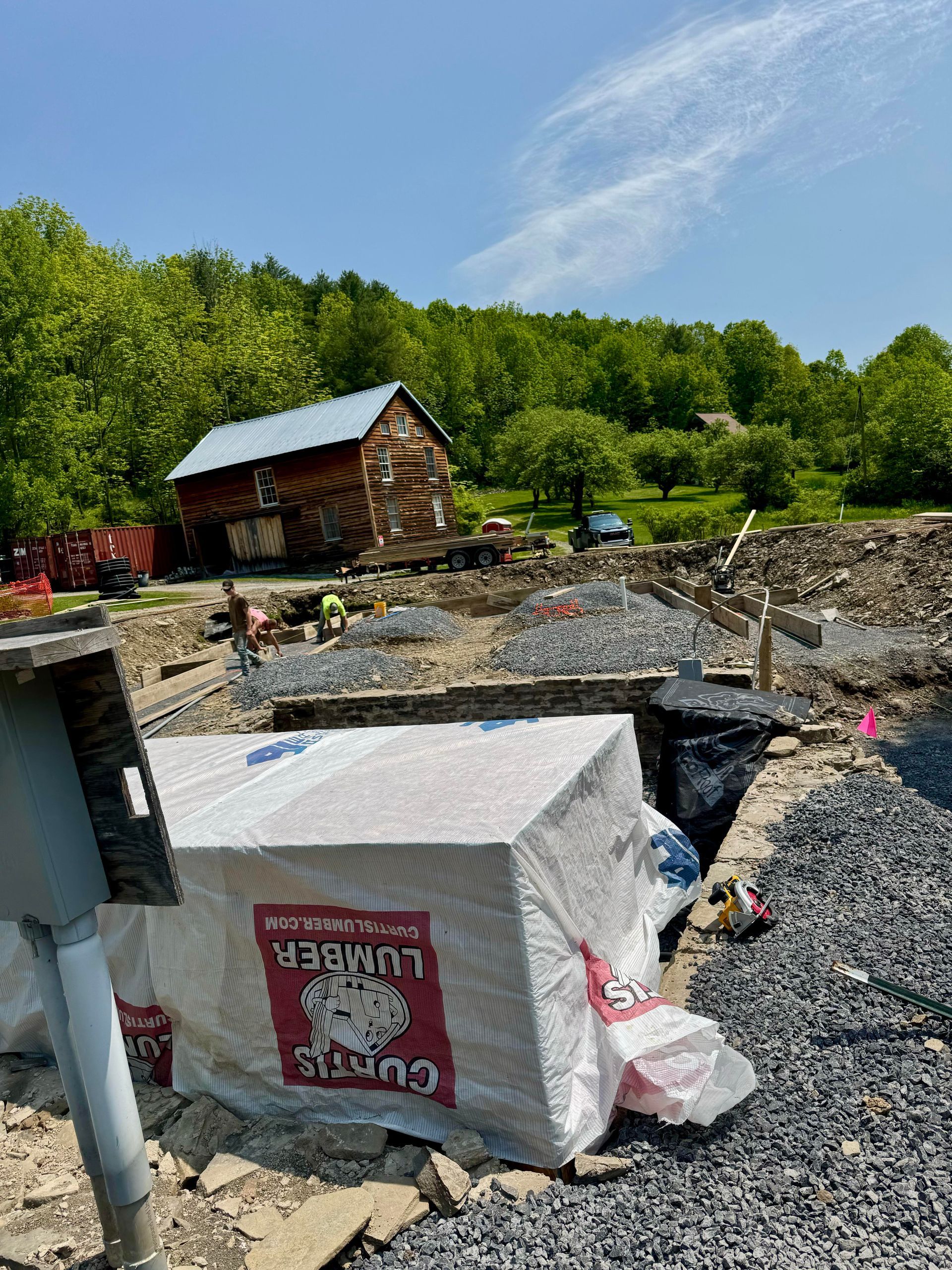 Construction site with building materials in foreground and small wooden structure in background, under a blue sky.