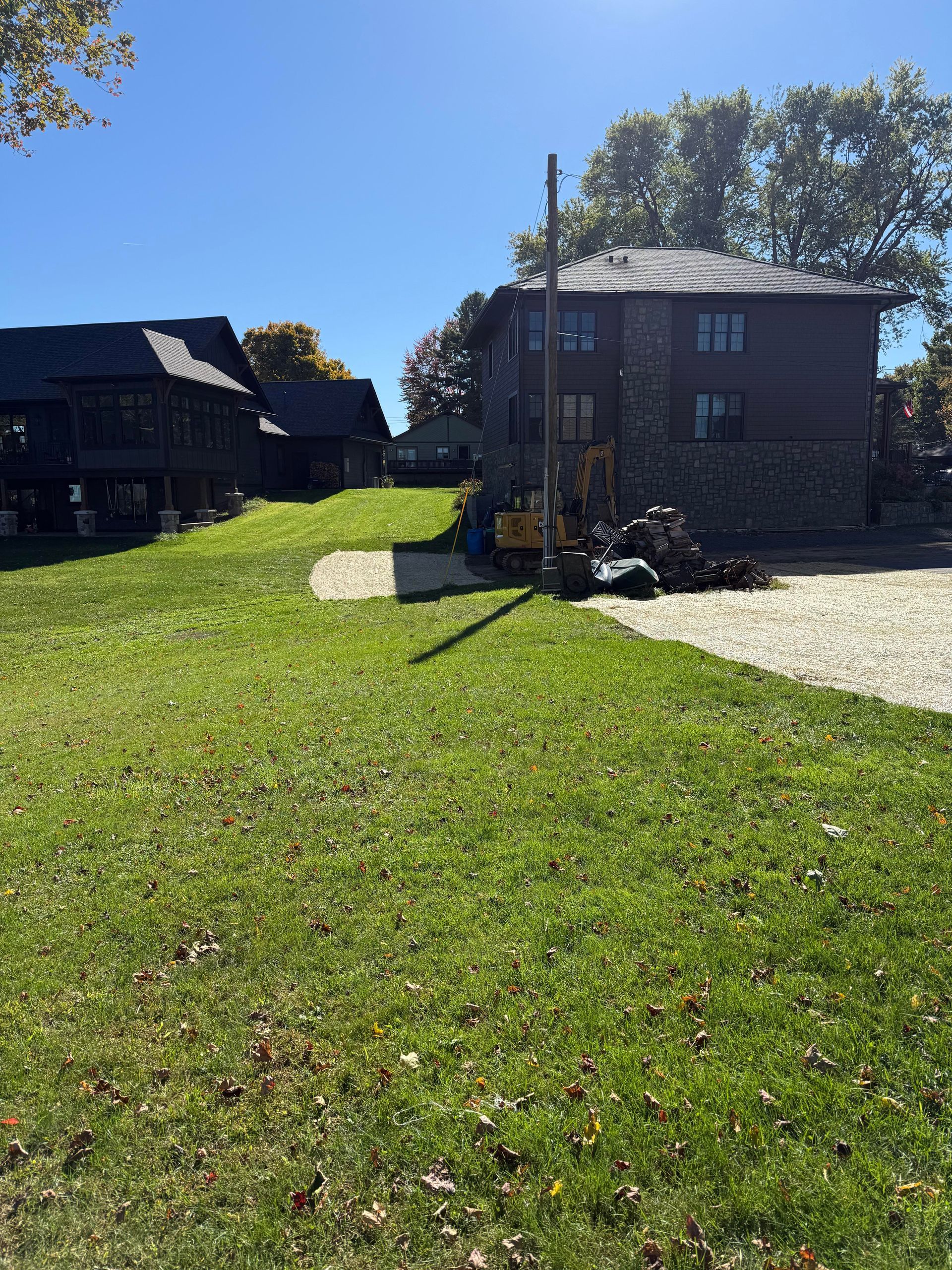 A utility pole is being installed next to a stone house on a grassy property.