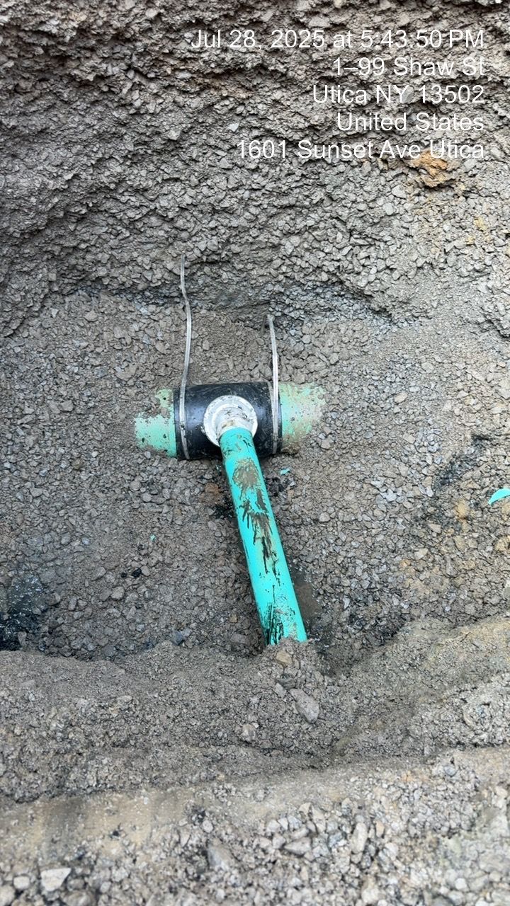 Green pipe and black coupling in a dirt excavation. Wires hold the coupling in place.