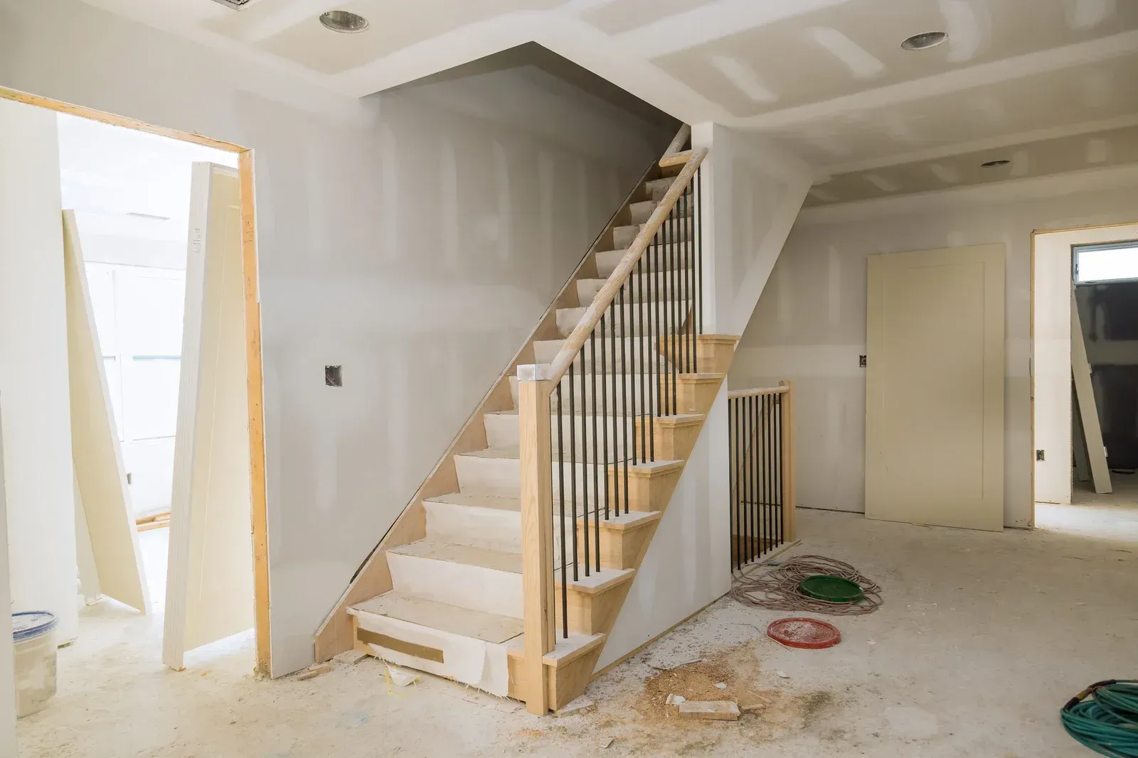 A staircase under construction inside a house. The wooden stairs have black metal railings, unfinished drywall on the walls.