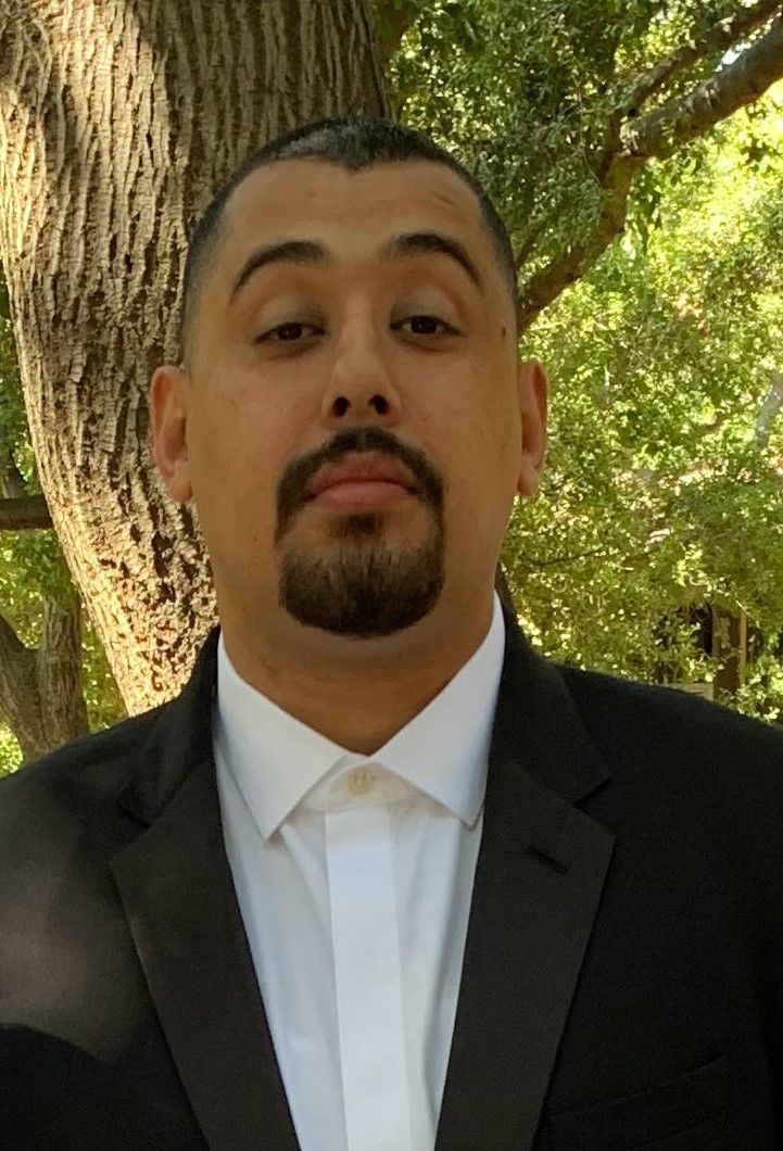 A man with a beard is wearing a suit and white shirt