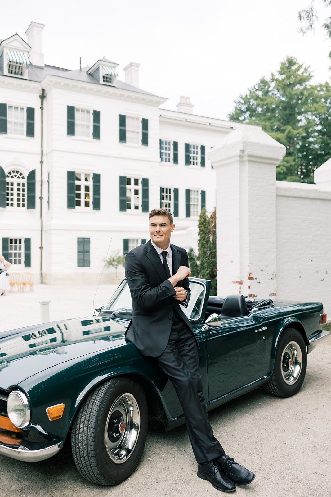 A man in a suit and tie is leaning on a green sports car.