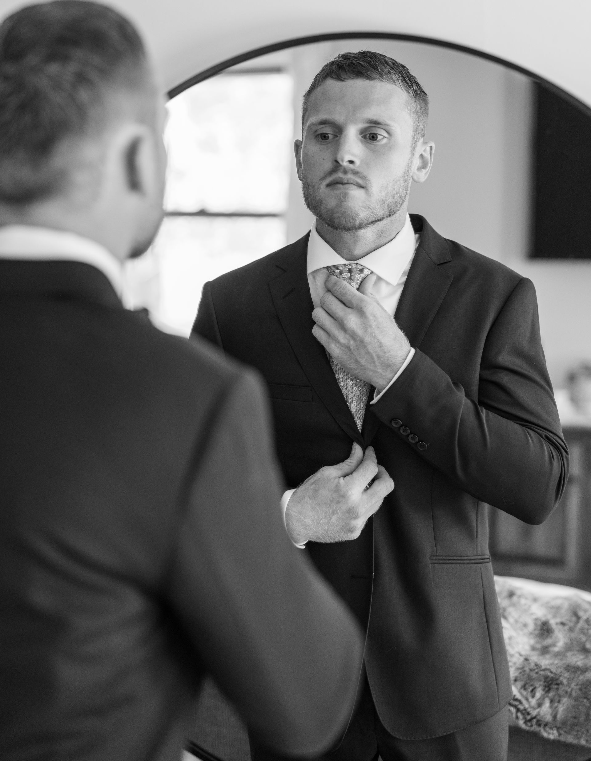 A man in a suit is adjusting his tie in front of a mirror.