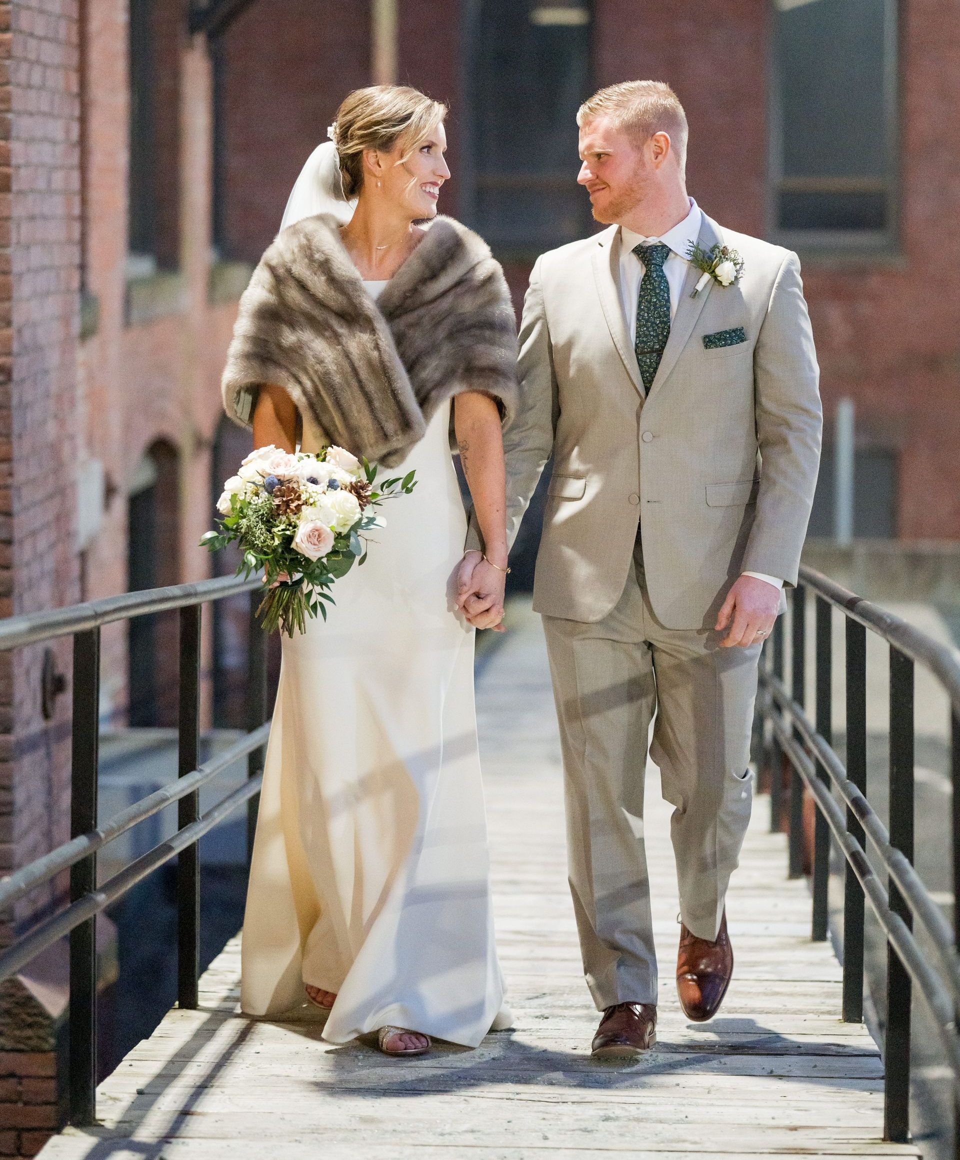 A bride and groom are walking across a bridge holding hands