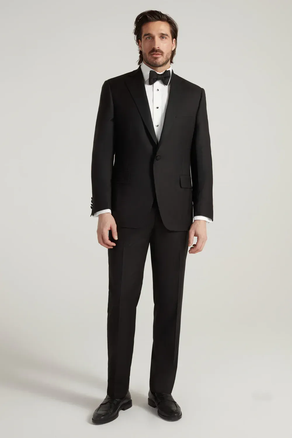 A man is wearing a black tuxedo and bow tie.