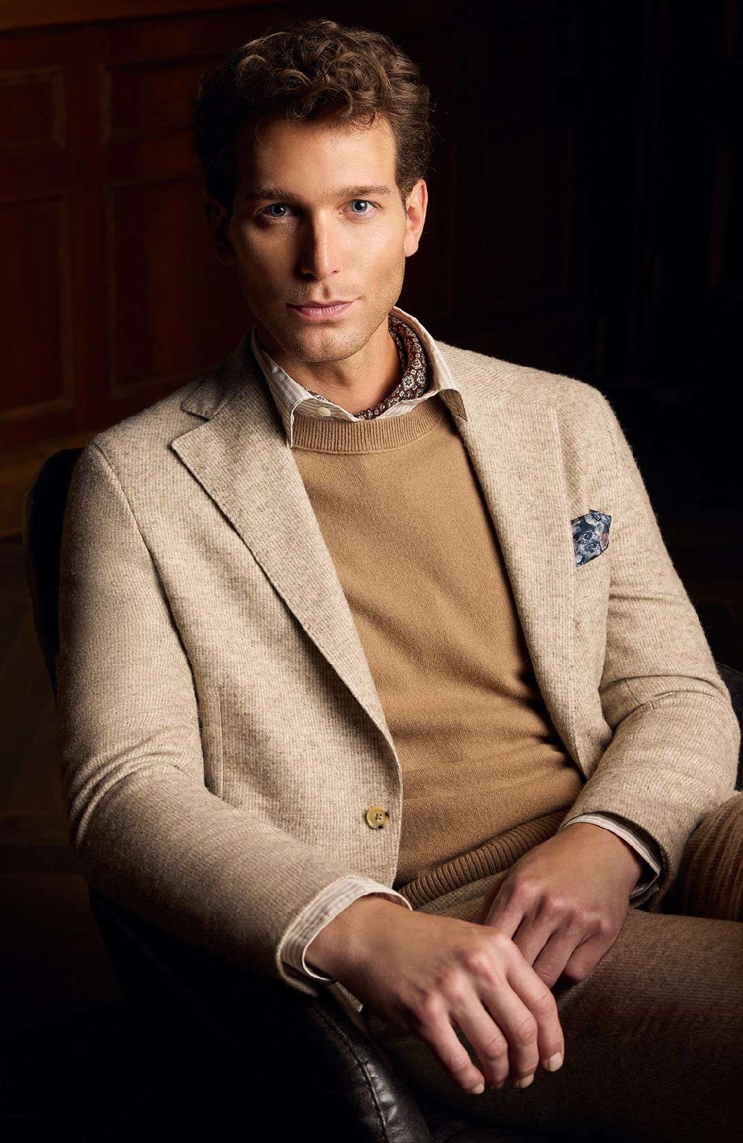 A man is sitting in a chair wearing a jacket and sweater.