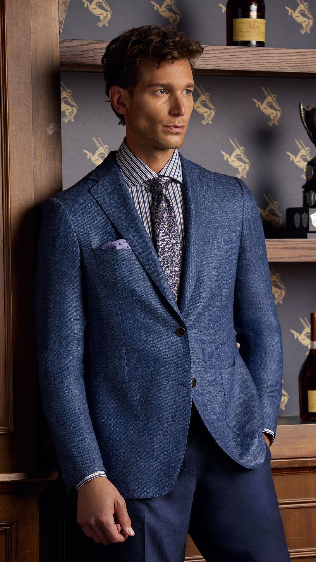 A man in a blue suit and tie is leaning against a wall.