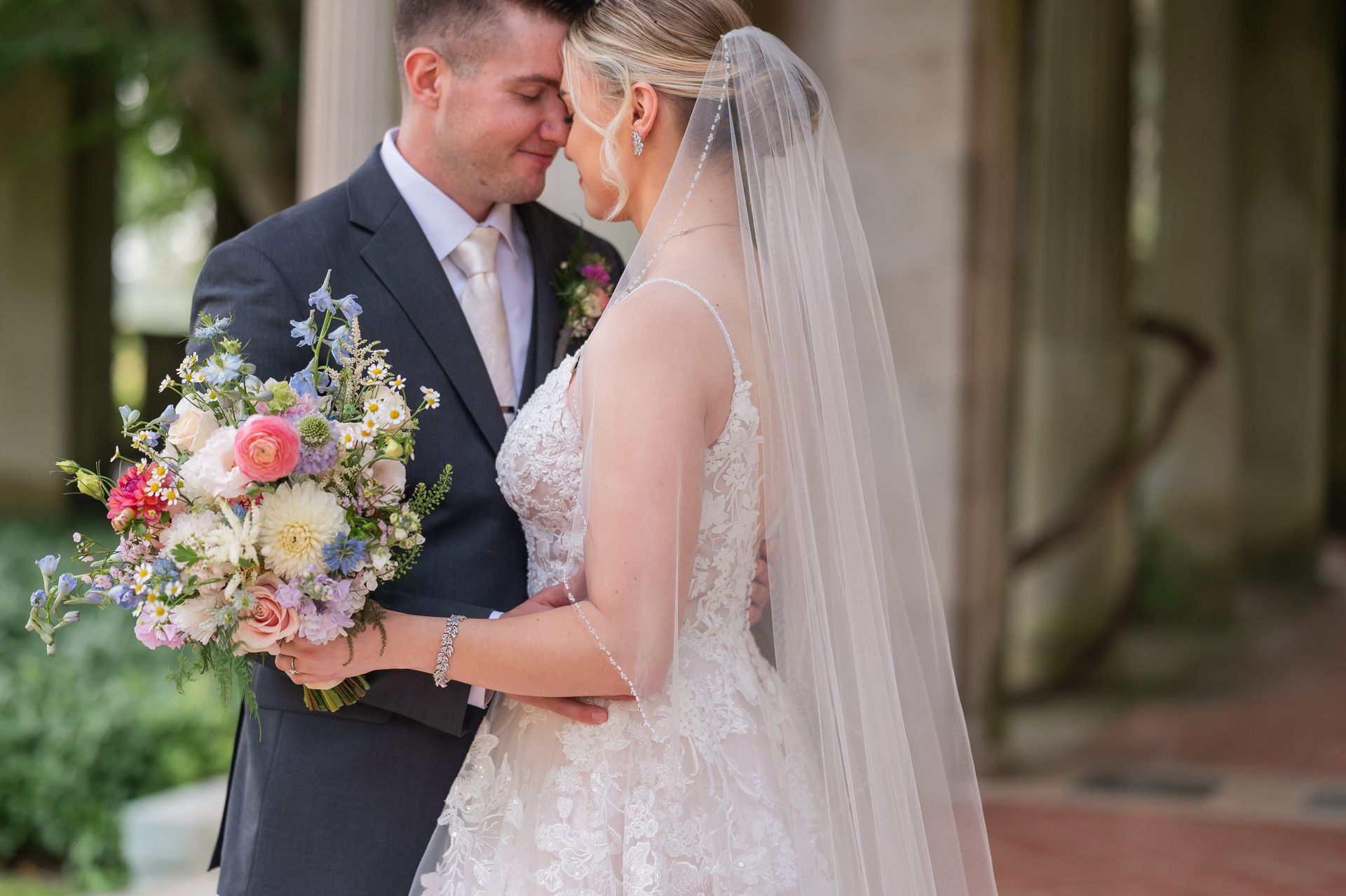 A bride and groom are kissing in front of a building while the bride is holding a bouquet of flowers.