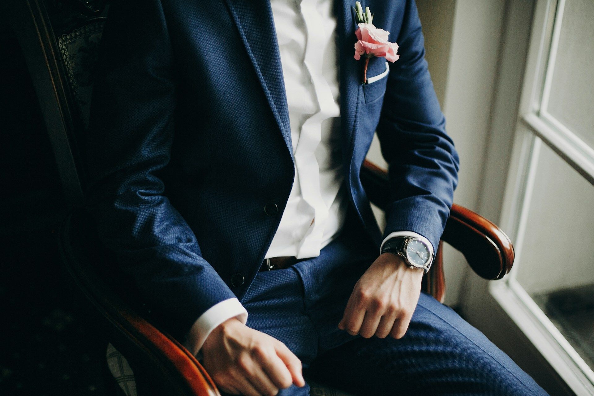 A man in a blue suit and tie is leaning against a wall.