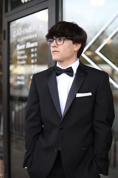 A young man in a tuxedo and bow tie is standing in front of a building.