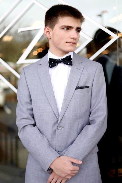 A young man in a suit and bow tie is standing in front of a window.