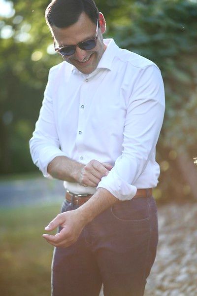 A man wearing sunglasses and a white shirt is adjusting his cuffs.
