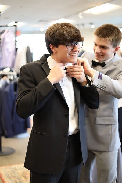 A man is helping another man put on a tuxedo.