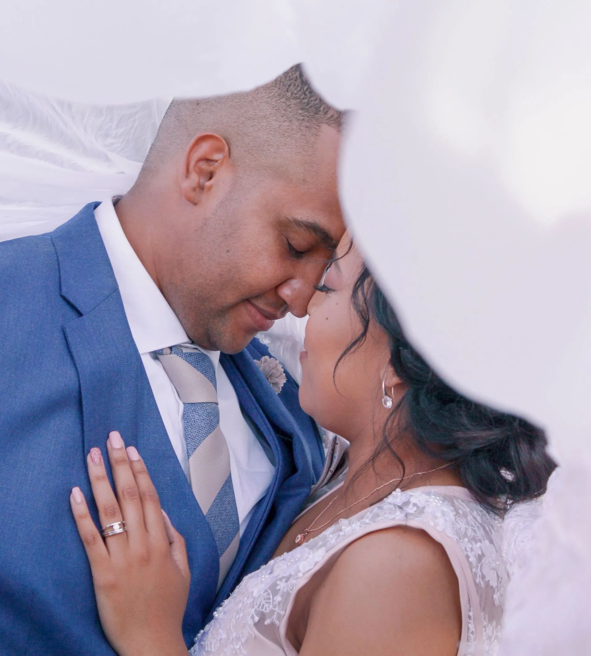 A bride and groom are kissing under an umbrella on their wedding day.