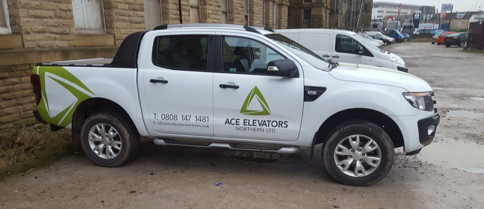 White pickup truck with company logo parked on a paved lot. A white van is parked nearby.