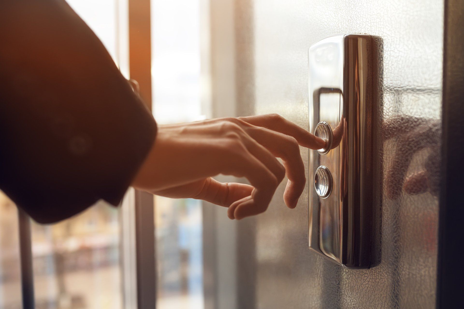 Person's hand pressing an elevator button. Close-up on the hand and control panel with sunlight in the background.