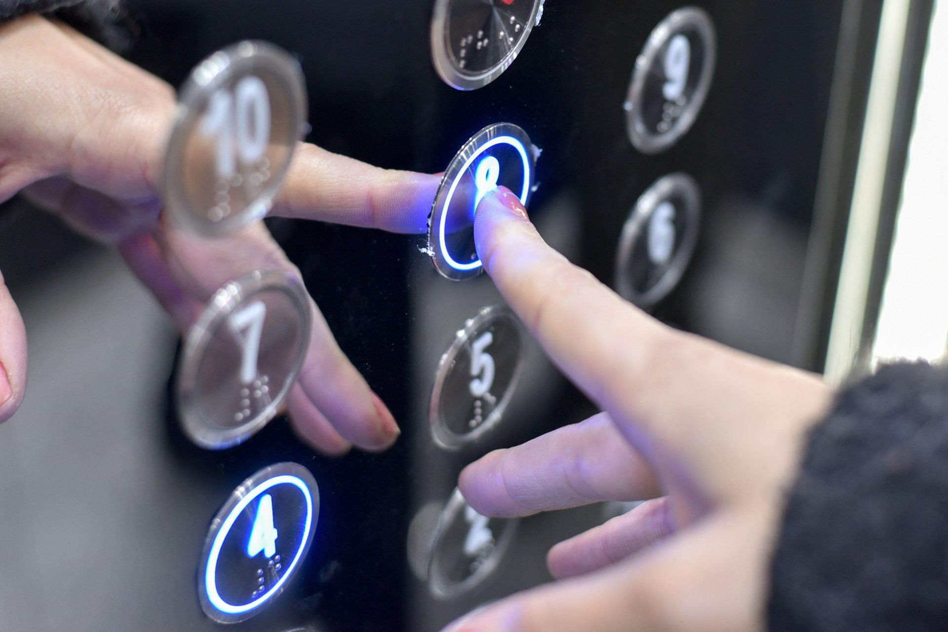 Hand presses illuminated button for floor 8 on an elevator panel.