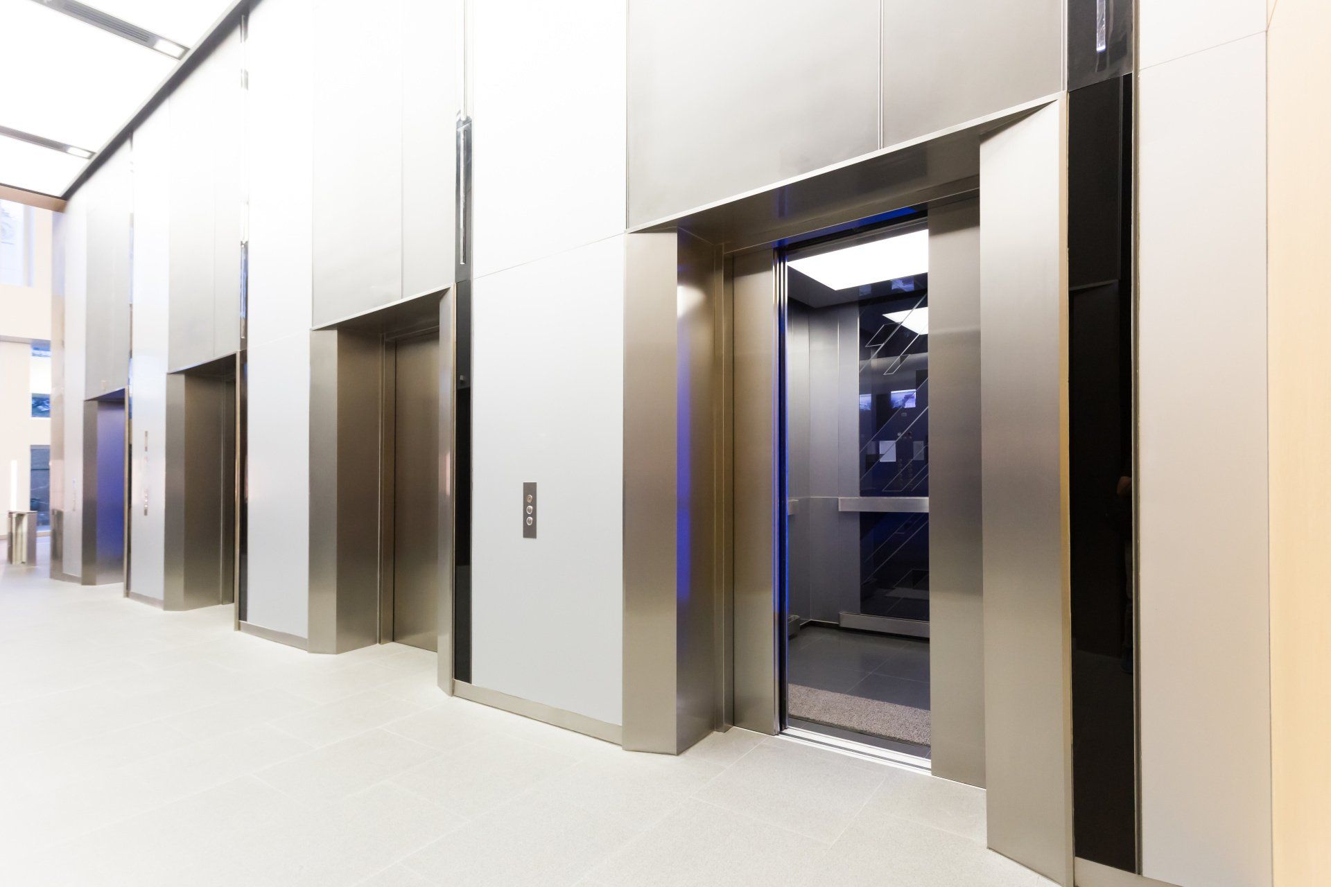 Elevator bank with stainless steel doors. One elevator is open, revealing the interior. Bright hallway.