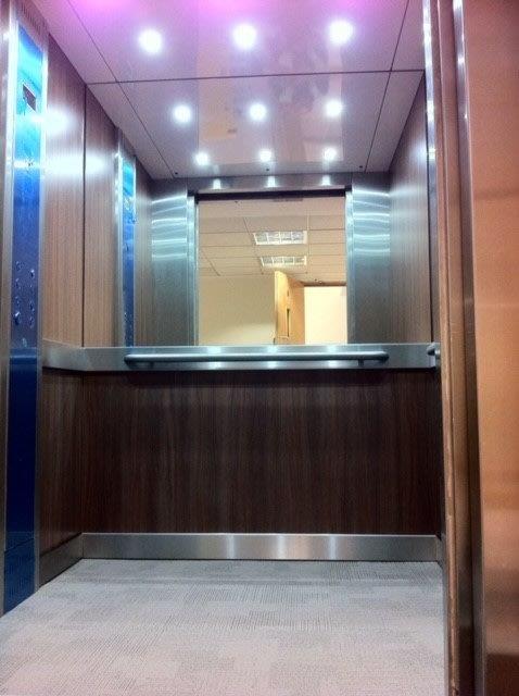Elevator interior with wood paneling, stainless steel accents, and a large mirror.