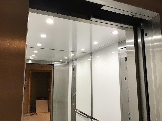 Elevator interior with white walls, glass panels, and a stainless steel frame. View from outside the open door.