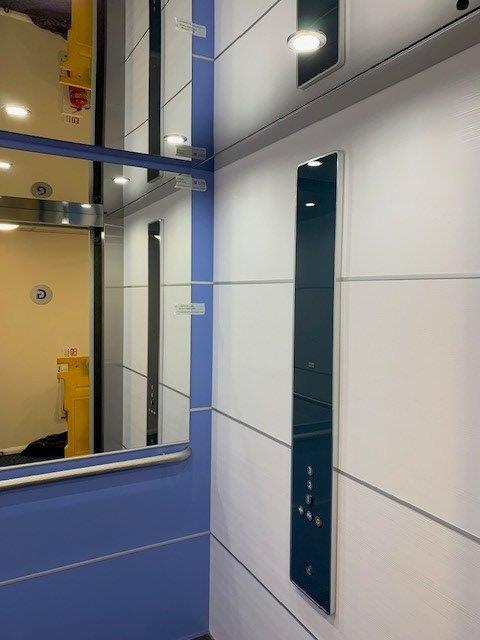 Interior view of an elevator with blue and white paneling, mirror, and control panel.
